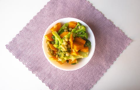 A vibrant mix of cooked vegetables including broccoli and carrots, served in a bowl on a textured mat.