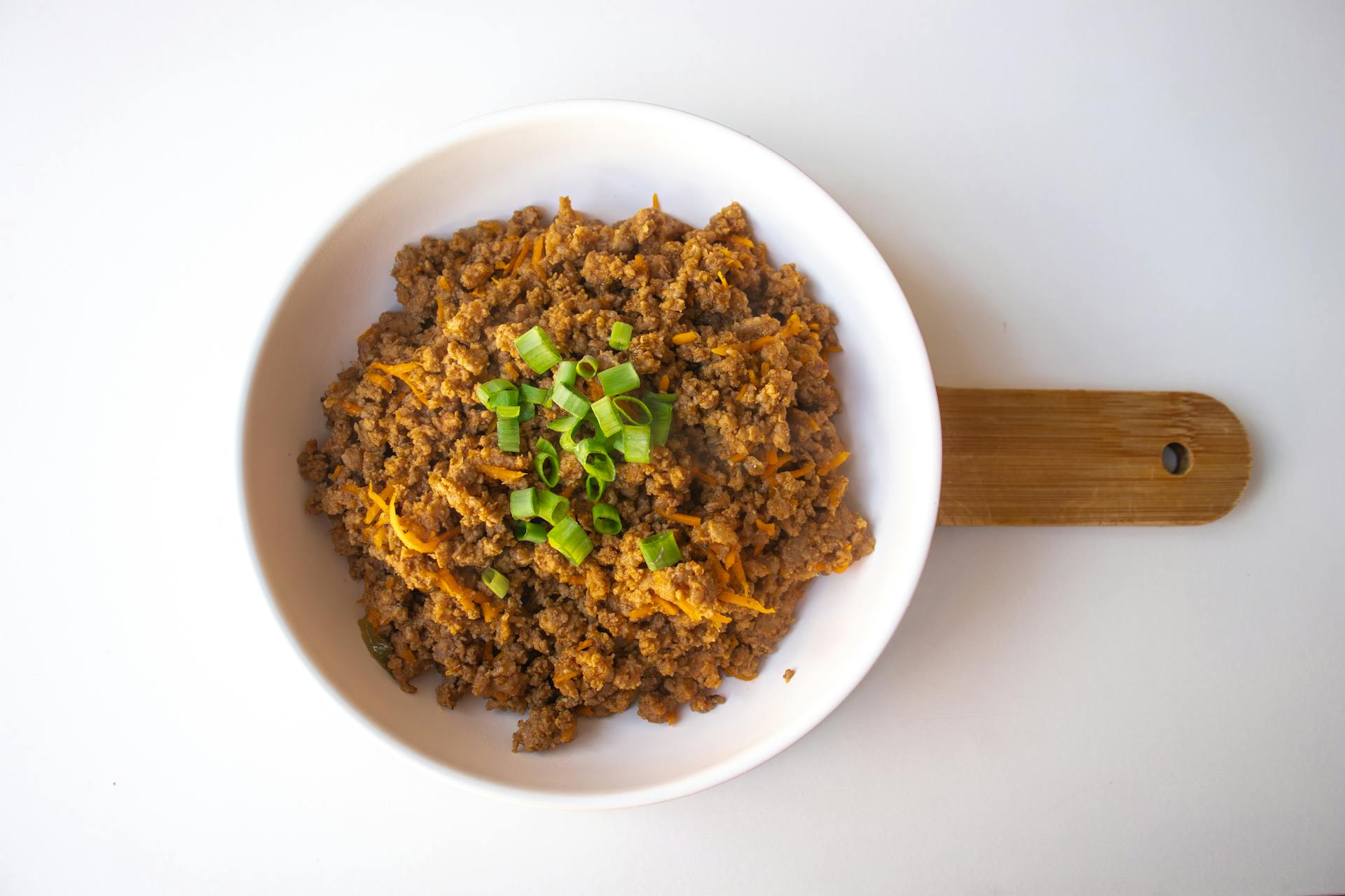 A flavorful bowl of seasoned ground beef garnished with cheese and green onions.