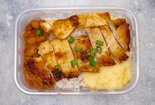Top view of a tasty home-cooked meal with grilled chicken, beans, and rice in a bento box.