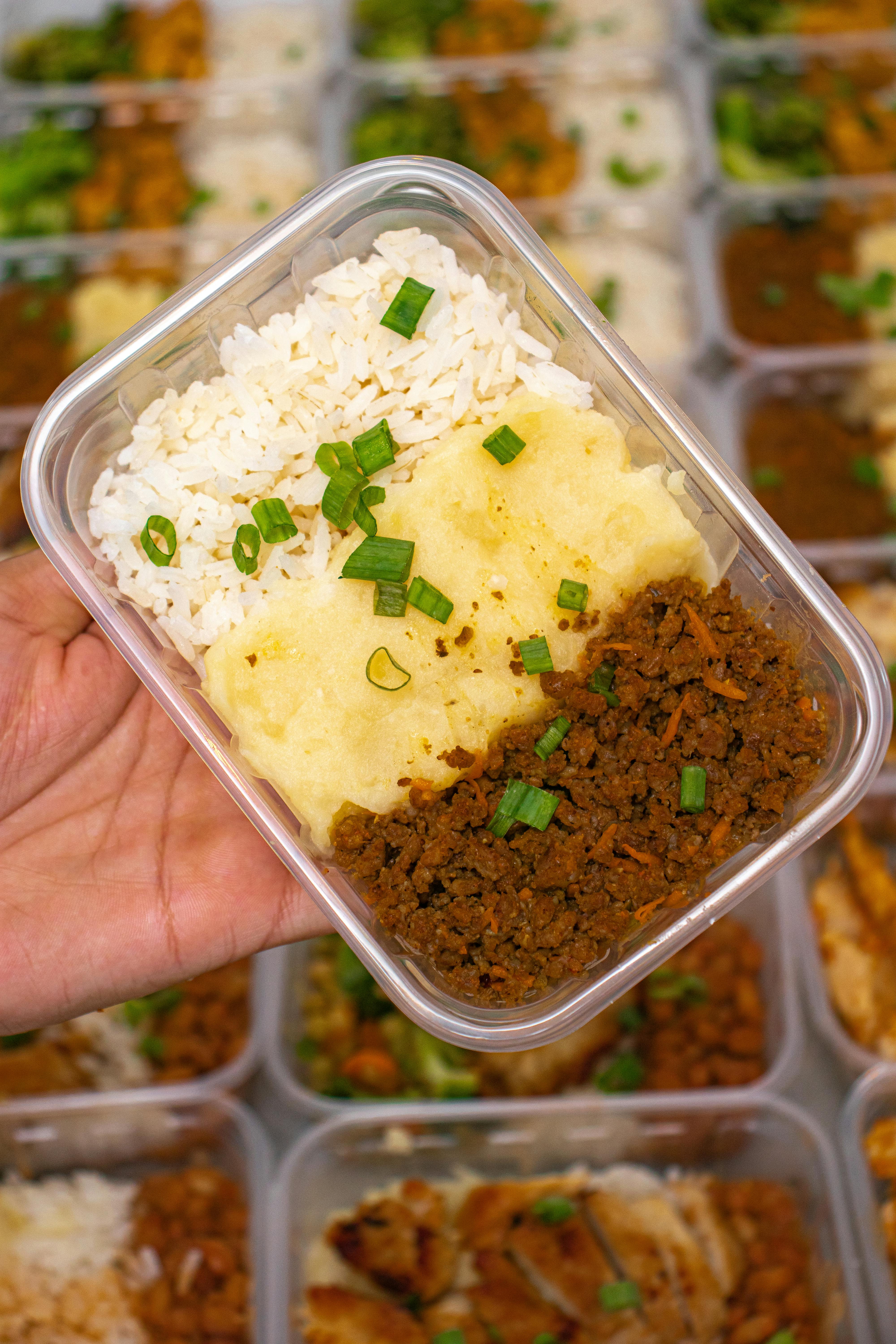 Hand holding meal prep box with rice, mashed potatoes, and ground beef. Ideal for healthy eating.