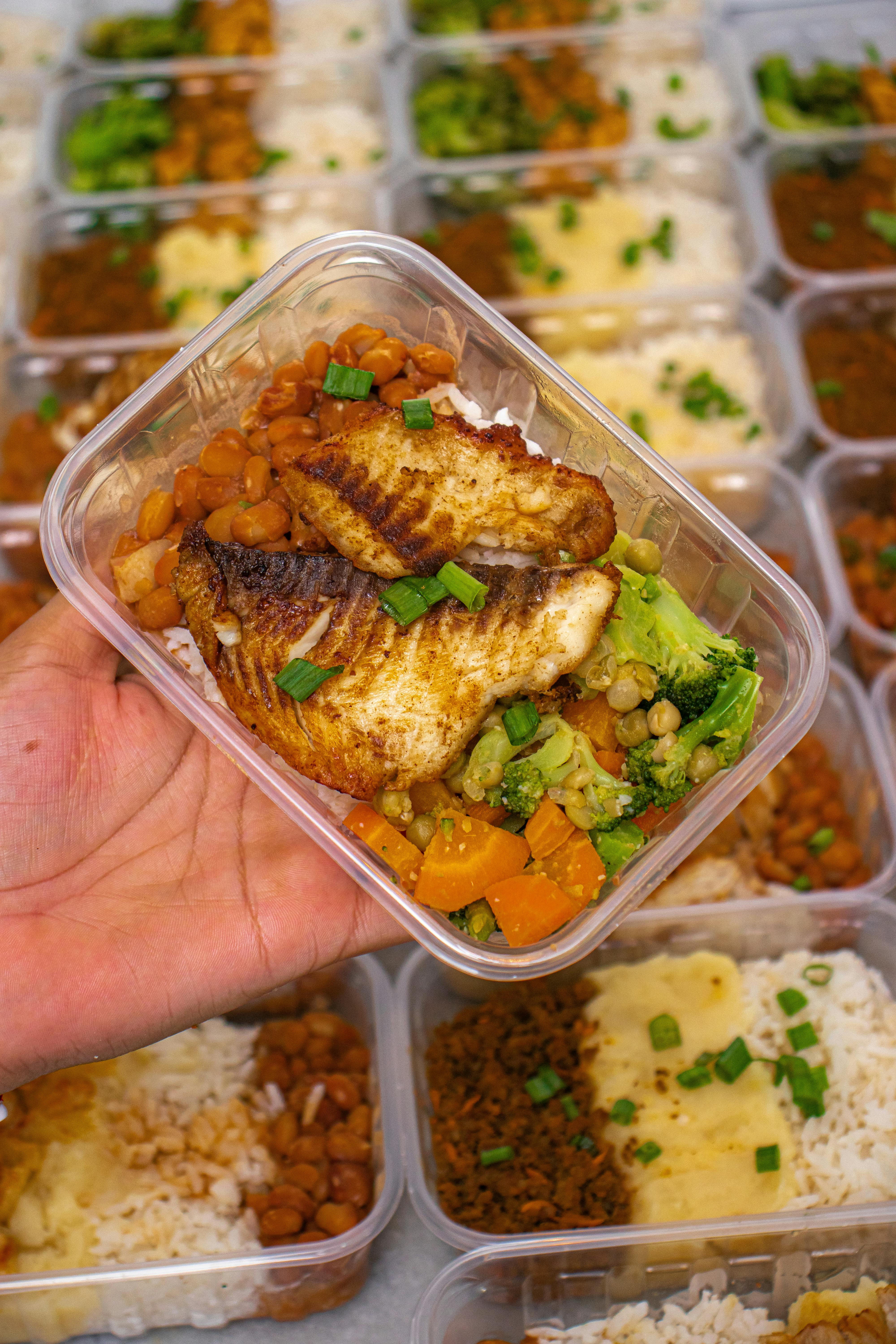 A nutritious meal prep box featuring grilled fish, broccoli, and beans for a balanced diet.