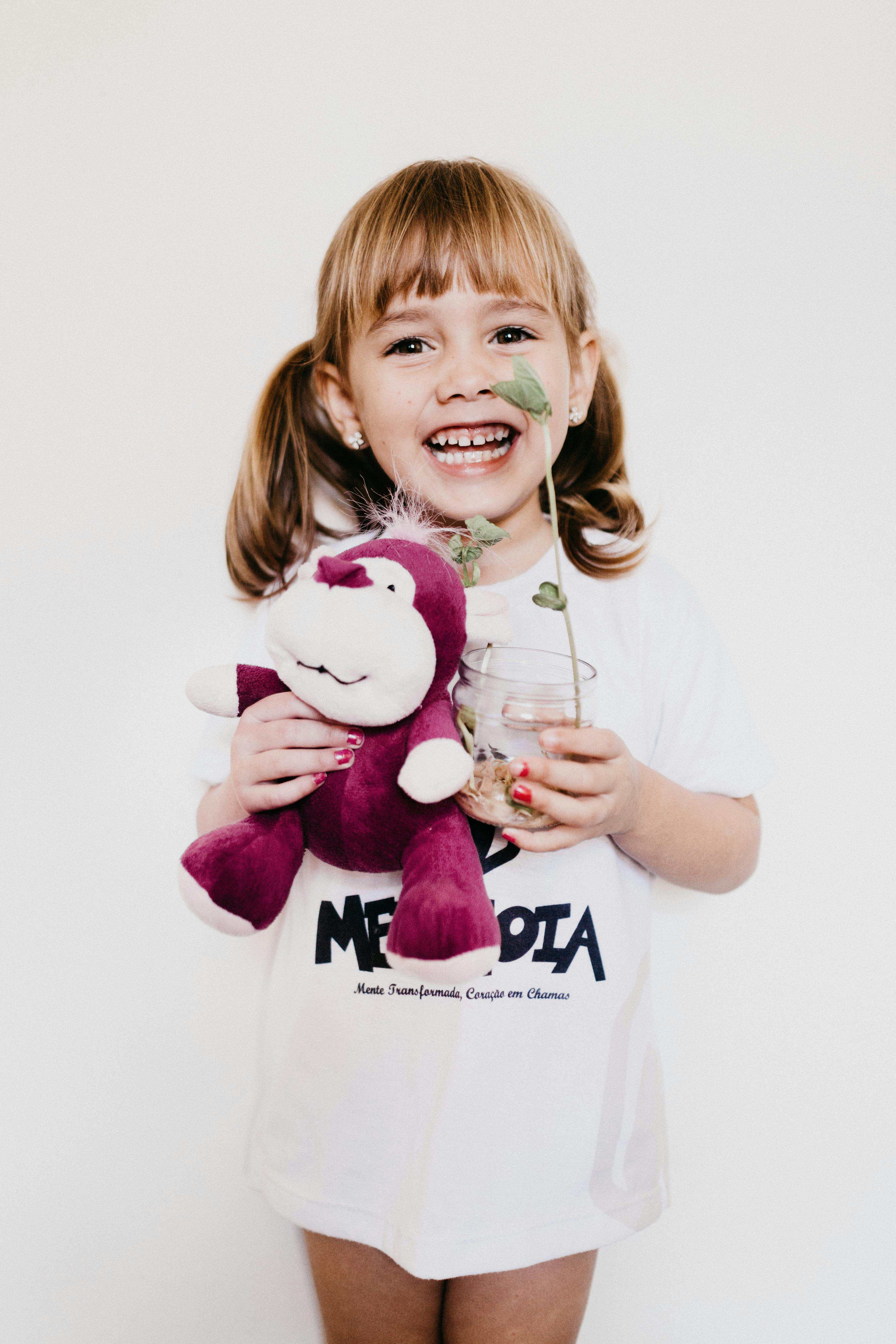 一个扎着辫子的快乐孩子，拿着紫色毛绒玩具和盆栽，笑容灿烂