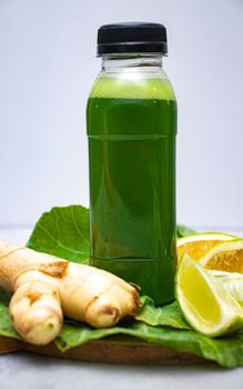 Vibrant green juice bottle with ginger and citrus slices on leafy background.