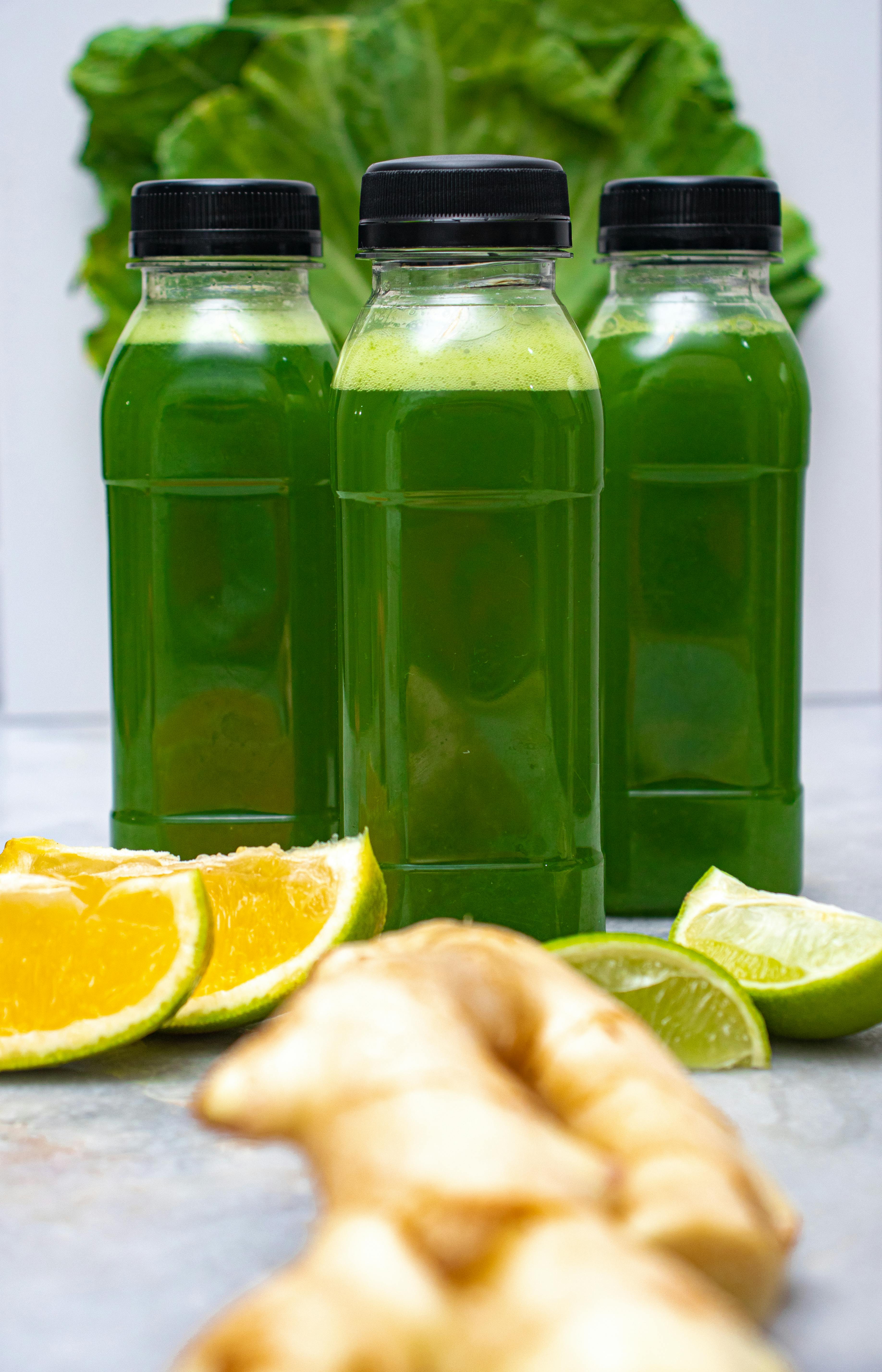 Three bottles of green juice surrounded by fresh citrus slices and ginger root for a healthy detox.