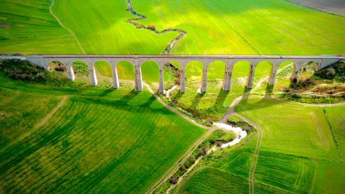 Free A stunning aerial view of a viaduct stretching across vibrant green fields, captured in daylight. Stock Photo
