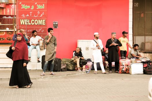 A bustling street scene in Saudi Arabia showing a diverse group of people waiting with luggage.