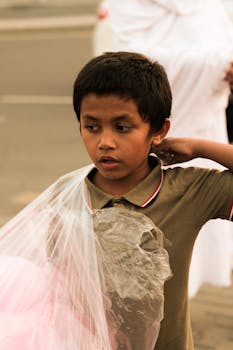A boy holding cotton candy on a street in Saudi Arabia, displaying a thoughtful expression.