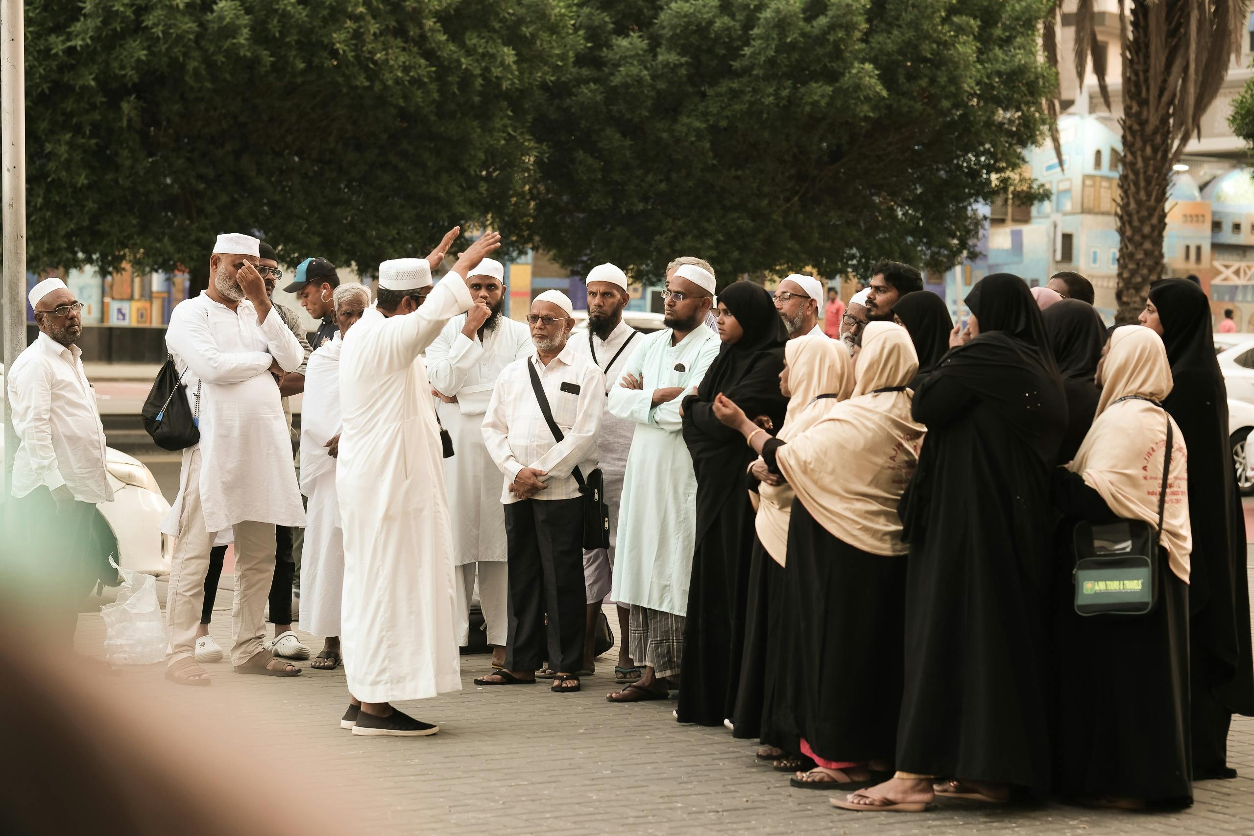 Free A group of pilgrims in traditional attire gather on a street in Saudi Arabia, engaging in discussion. Stock Photo