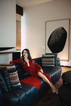 A stylish woman in a red dress posing on a blue sofa in a modern interior setting.