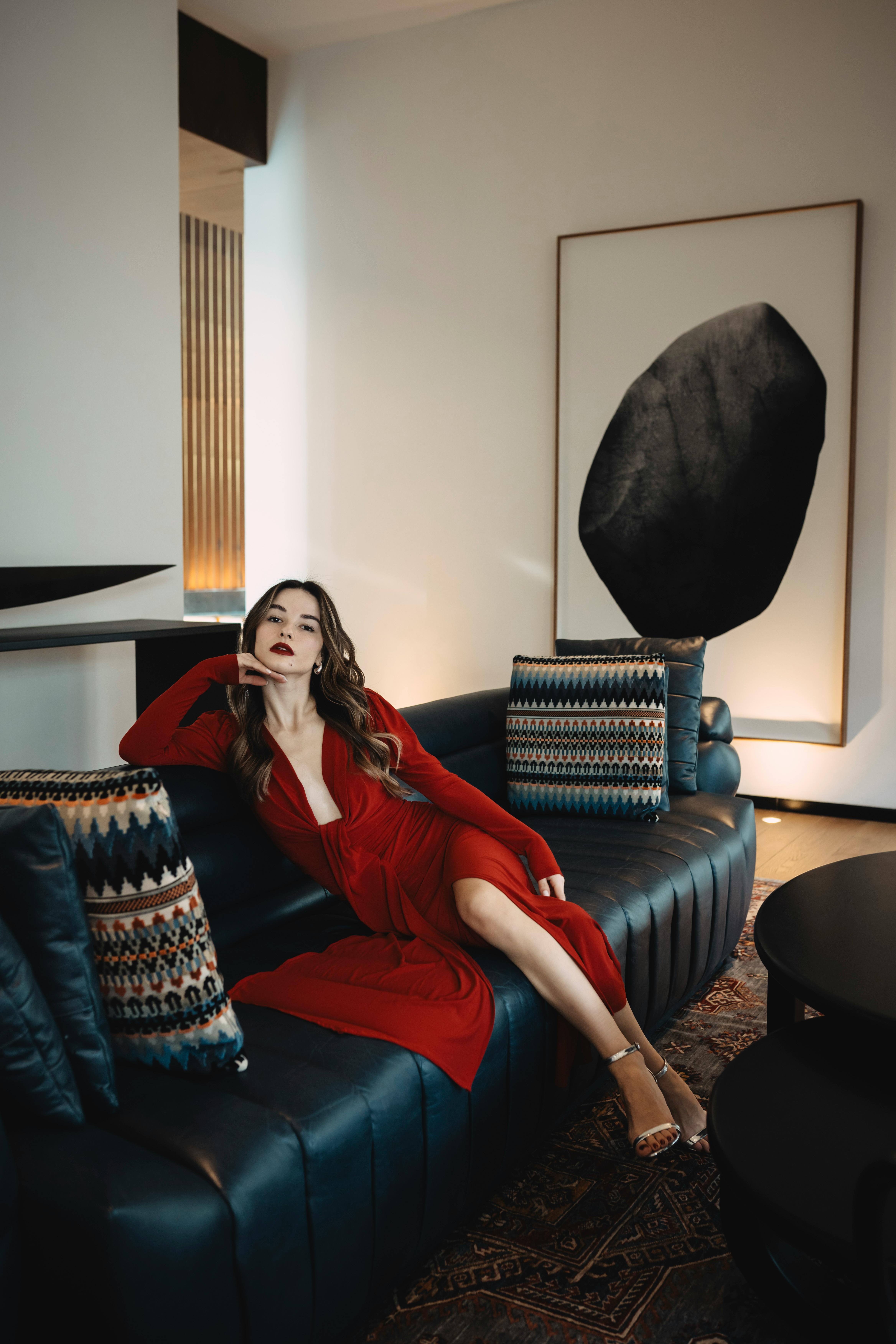 Elegant woman in a red dress reclines on a modern sofa in stylish room interior.