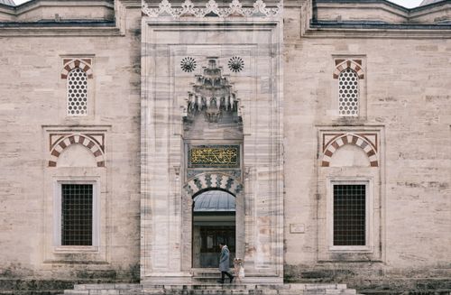 Free Elegant historic facade with arches, a woman stands in front, showcasing classic Middle Eastern architecture. Stock Photo