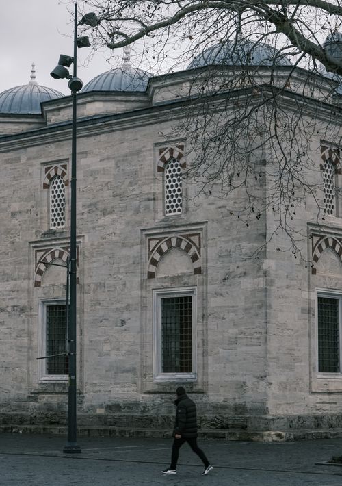 Free A person walks near an old stone building with distinct architectural features. Stock Photo