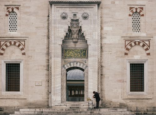 Free A man cleaning at the grand entrance of a historic mosque with intricate Arabic calligraphy. Stock Photo
