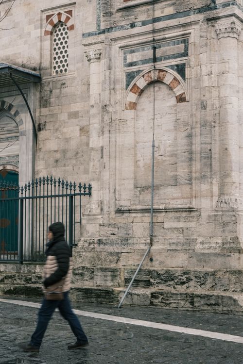 Free A blurred pedestrian walking past an ancient stone wall with intricate architecture details. Stock Photo