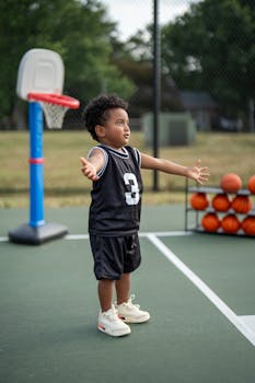 A young child playing basketball on an outdoor court, wearing a black jersey.