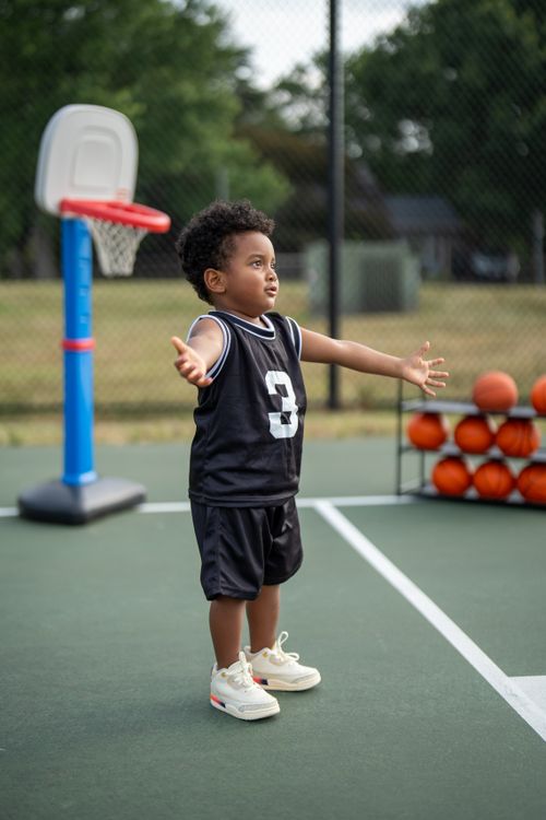 Free A young child playing basketball on an outdoor court, wearing a black jersey. Stock Photo