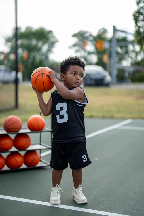 Free Young boy holding basketball on outdoor court, ready to play. Stock Photo