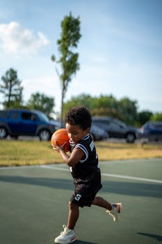 A young boy playing basketball on an outdoor court during a sunny day.