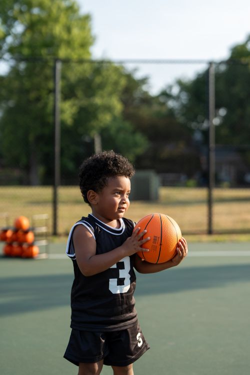 Free A young boy in a black jersey plays on an outdoor basketball court during the day. Stock Photo