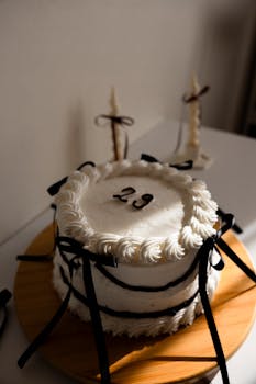Stylish 29th birthday cake with black ribbons and white frosting on display.