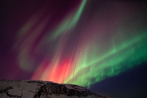 Free Vibrant aurora borealis dances over snowy mountains in Iceland, showcasing stunning night sky colors. Stock Photo