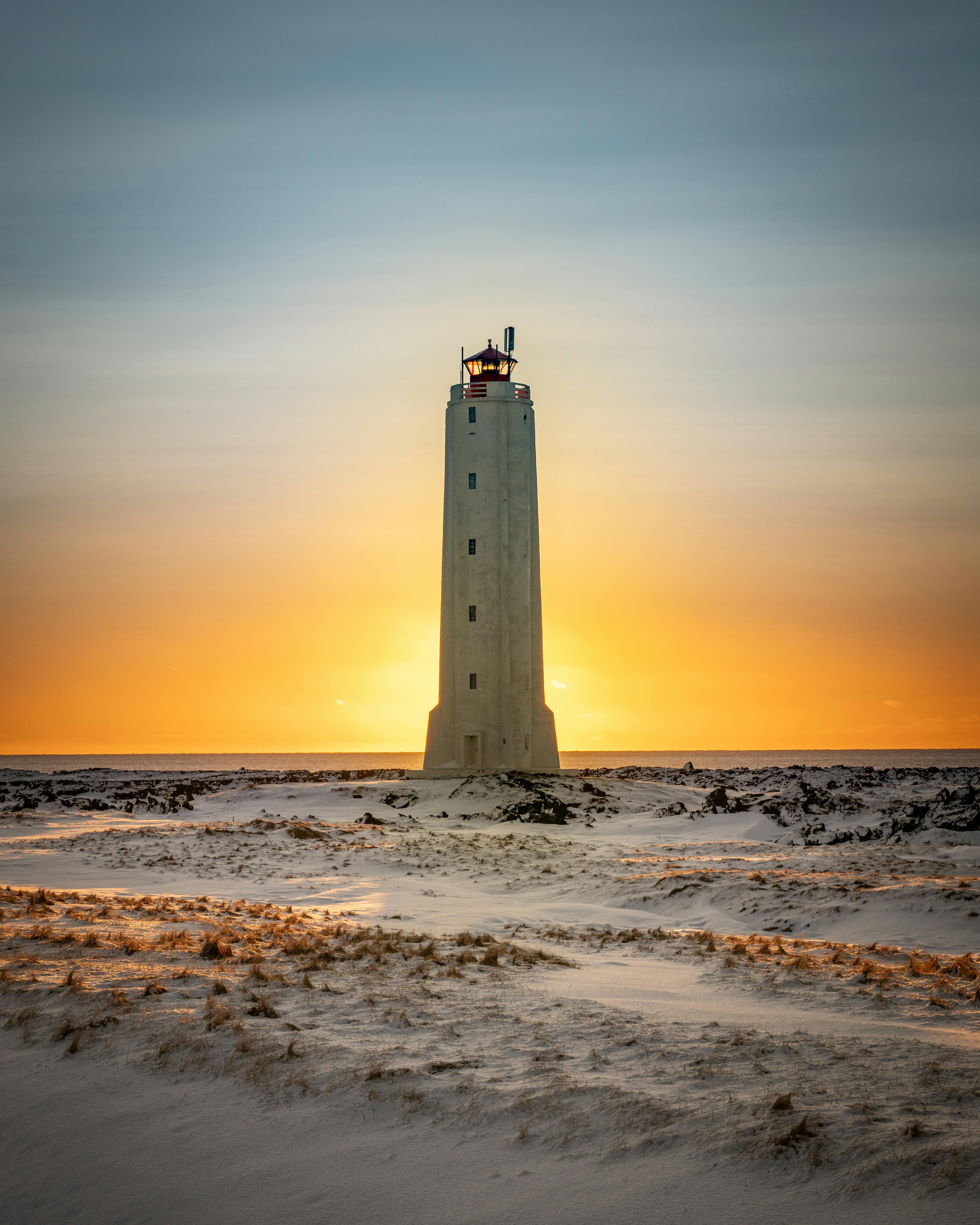 A breathtaking sunset behind a lighthouse on a snowy Icelandic landscape, creating a dramatic scene.