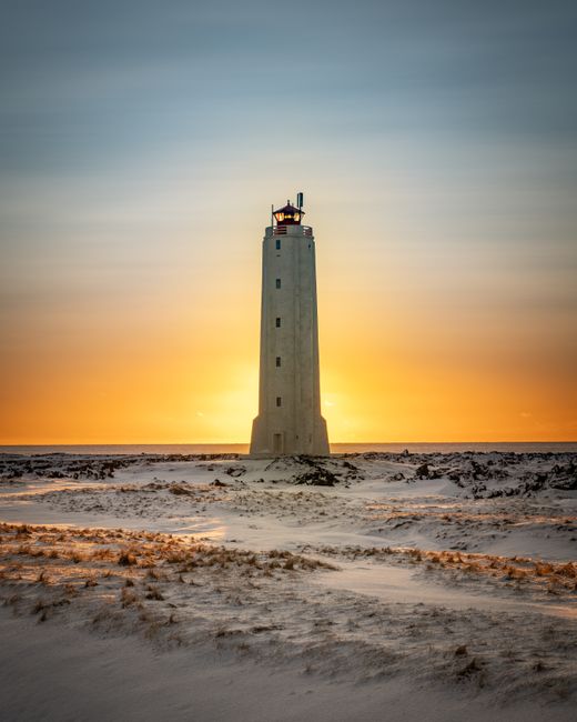 A breathtaking sunset behind a lighthouse on a snowy Icelandic landscape, creating a dramatic scene.