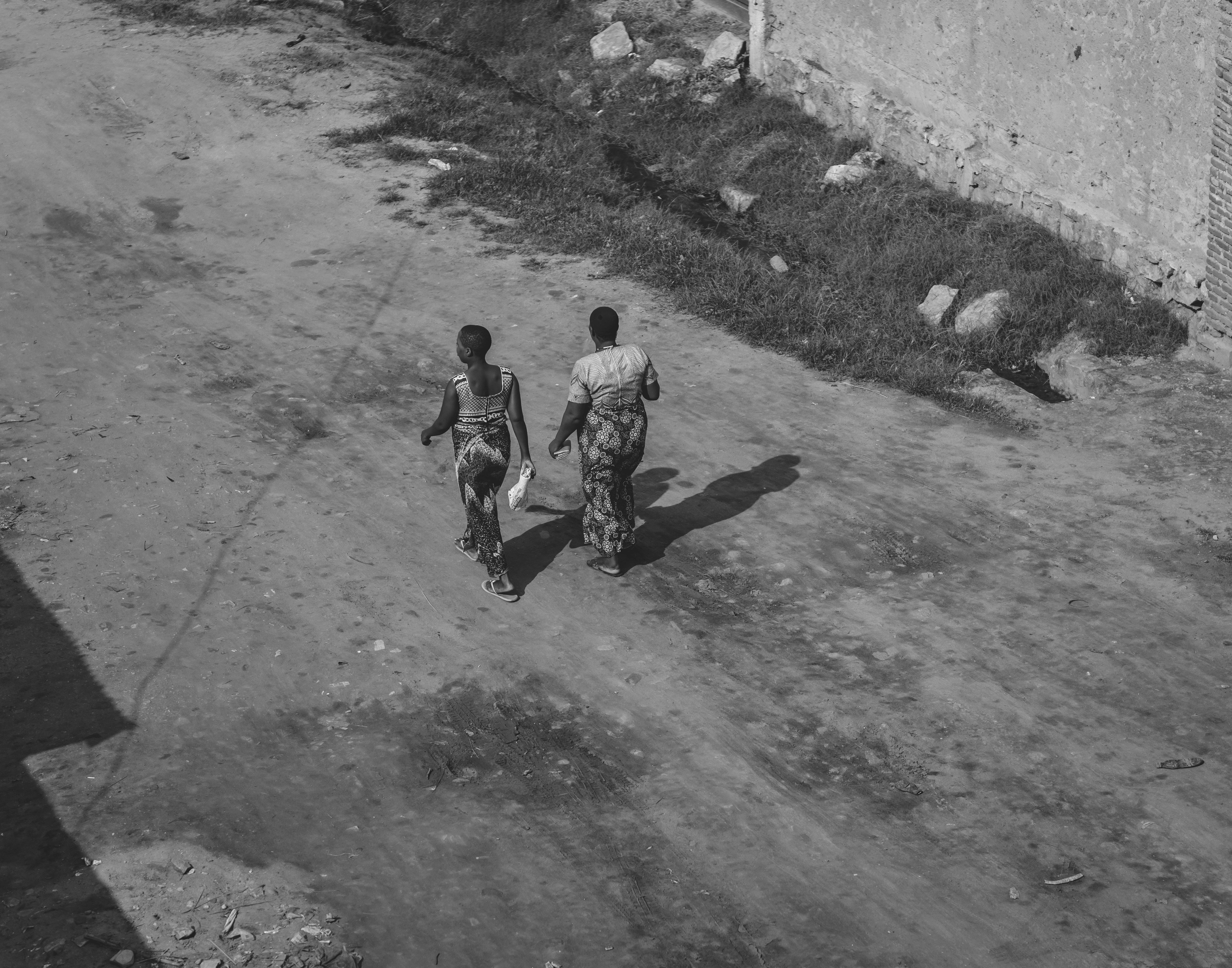 Black and white photo of two people walking down a dirt road in a rural area.