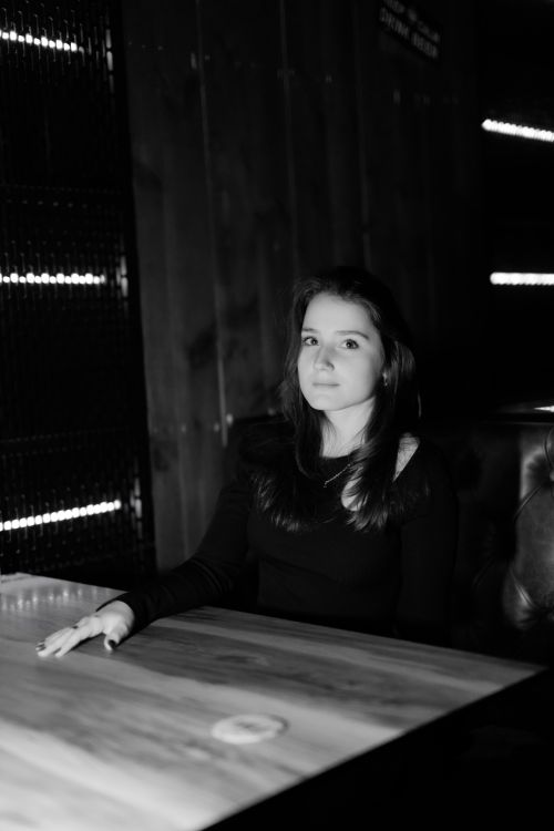 Free Black and white portrait of a woman sitting at a table in a dimly lit room. Stock Photo