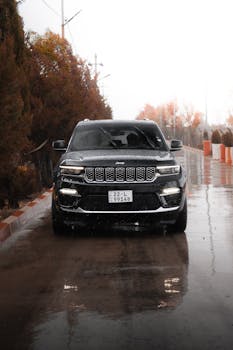 A Jeep SUV drives on a wet road in Erbil, Iraq, surrounded by autumn foliage.