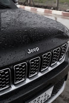 A detailed view of a black Jeep SUV parked outdoors, showcasing rain droplets on the hood.