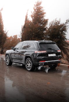 A black SUV driving on a wet road surrounded by autumn trees, showcasing off-road capabilities.