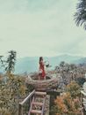 一名身穿红色连衣裙的女子，站在以风景优美的山为背景的大鸟巢里