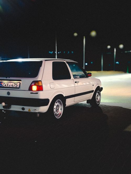 Free Stylish white retro hatchback parked under streetlights at night. Stock Photo