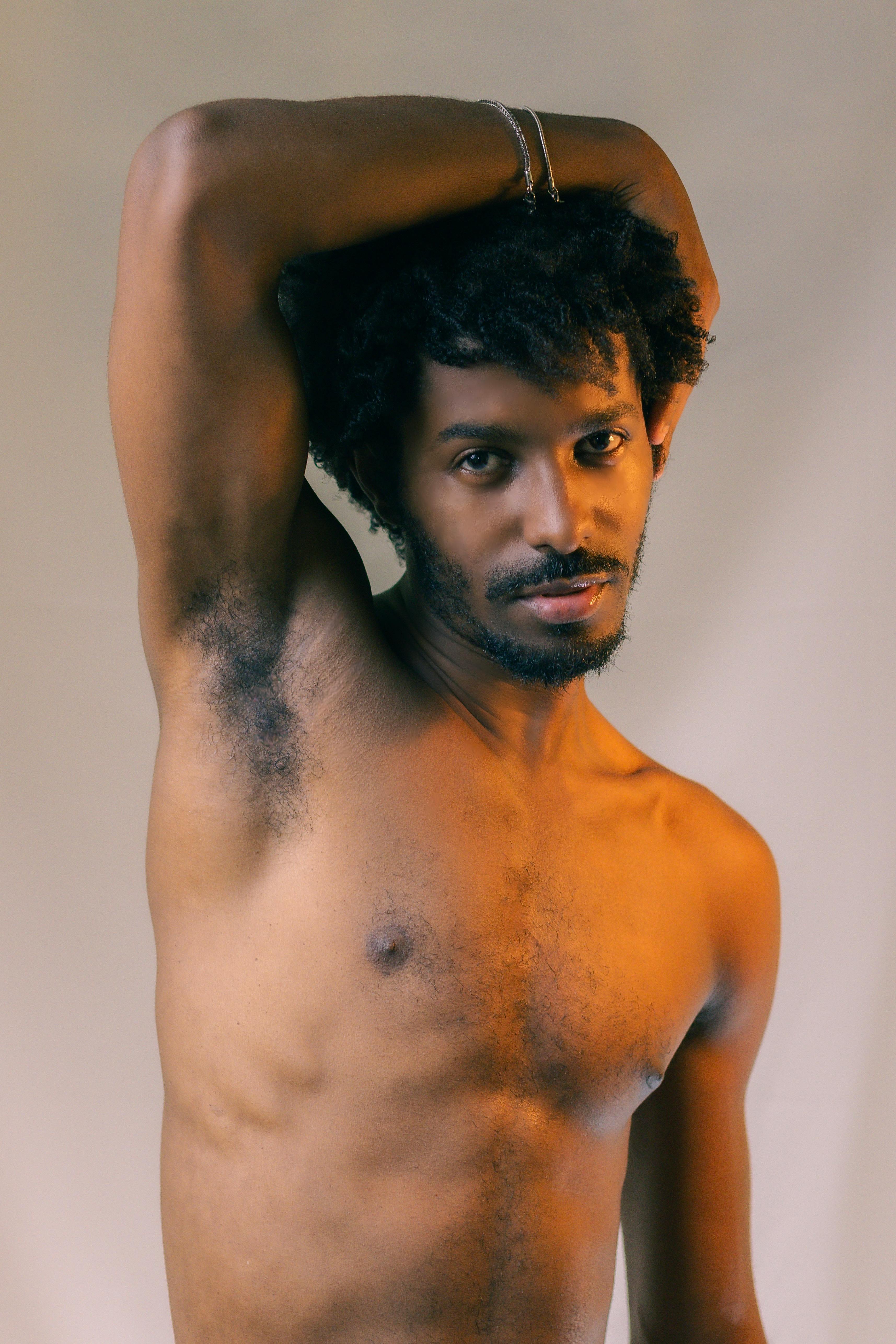 무료 윗옷을 벗은 남자가 팔을 들고 포즈를 취하며 자신감과 따뜻함을 보여준다. 스톡 사진