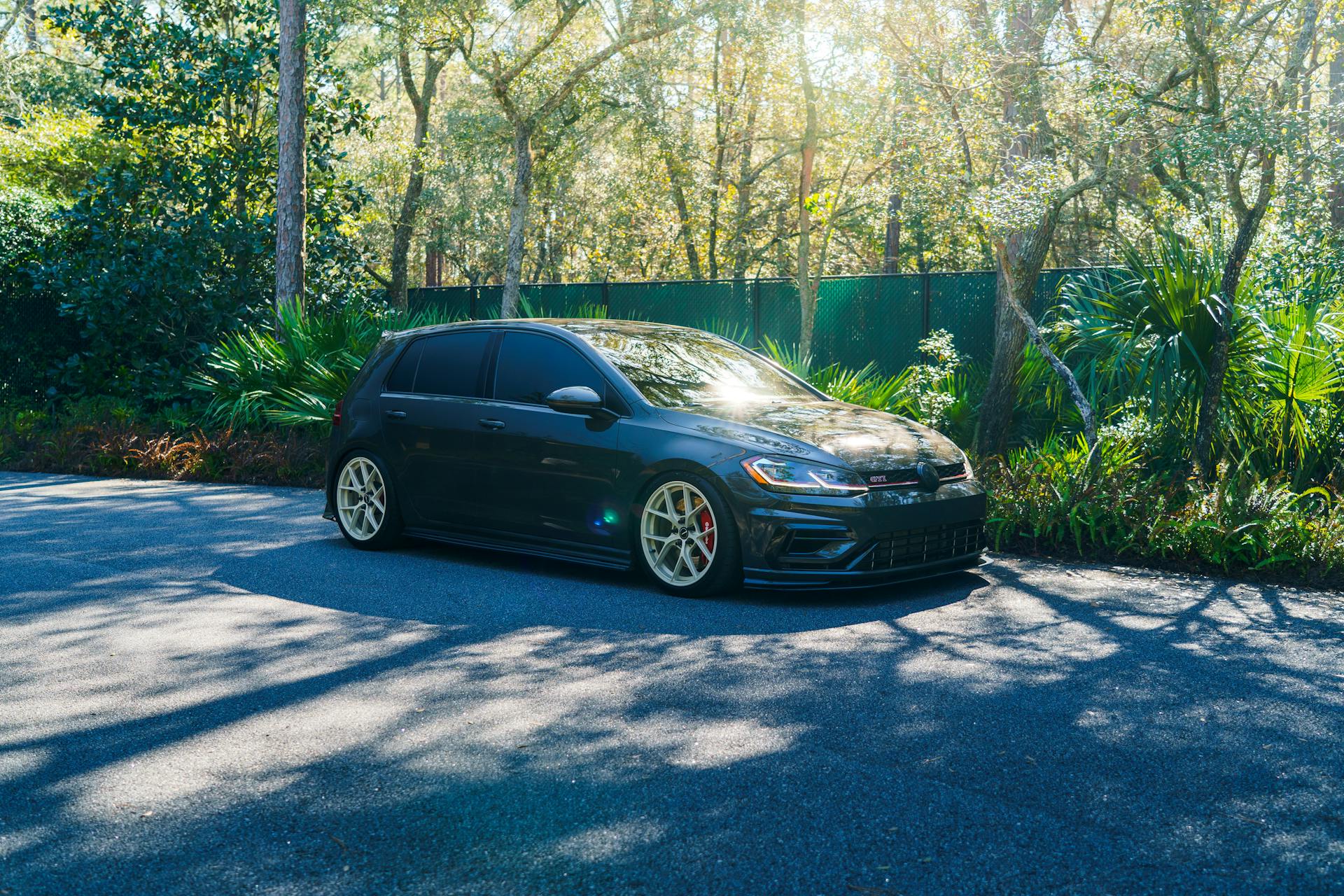 A sleek black car parked on a sunlit road surrounded by lush forest greenery.