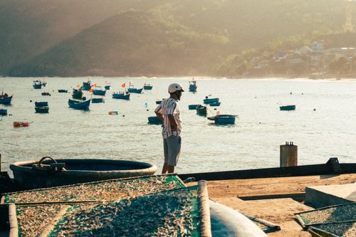 Free A man in a helmet stands by fishing boats in the scenic harbor of Quy Nhơn, Việt Nam. Stock Photo