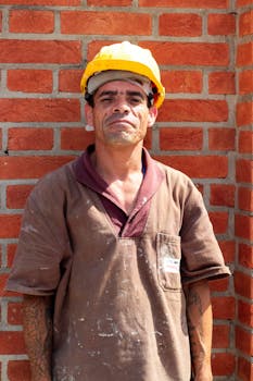 Portrait of a construction worker with hard hat standing against a brick wall outdoors.