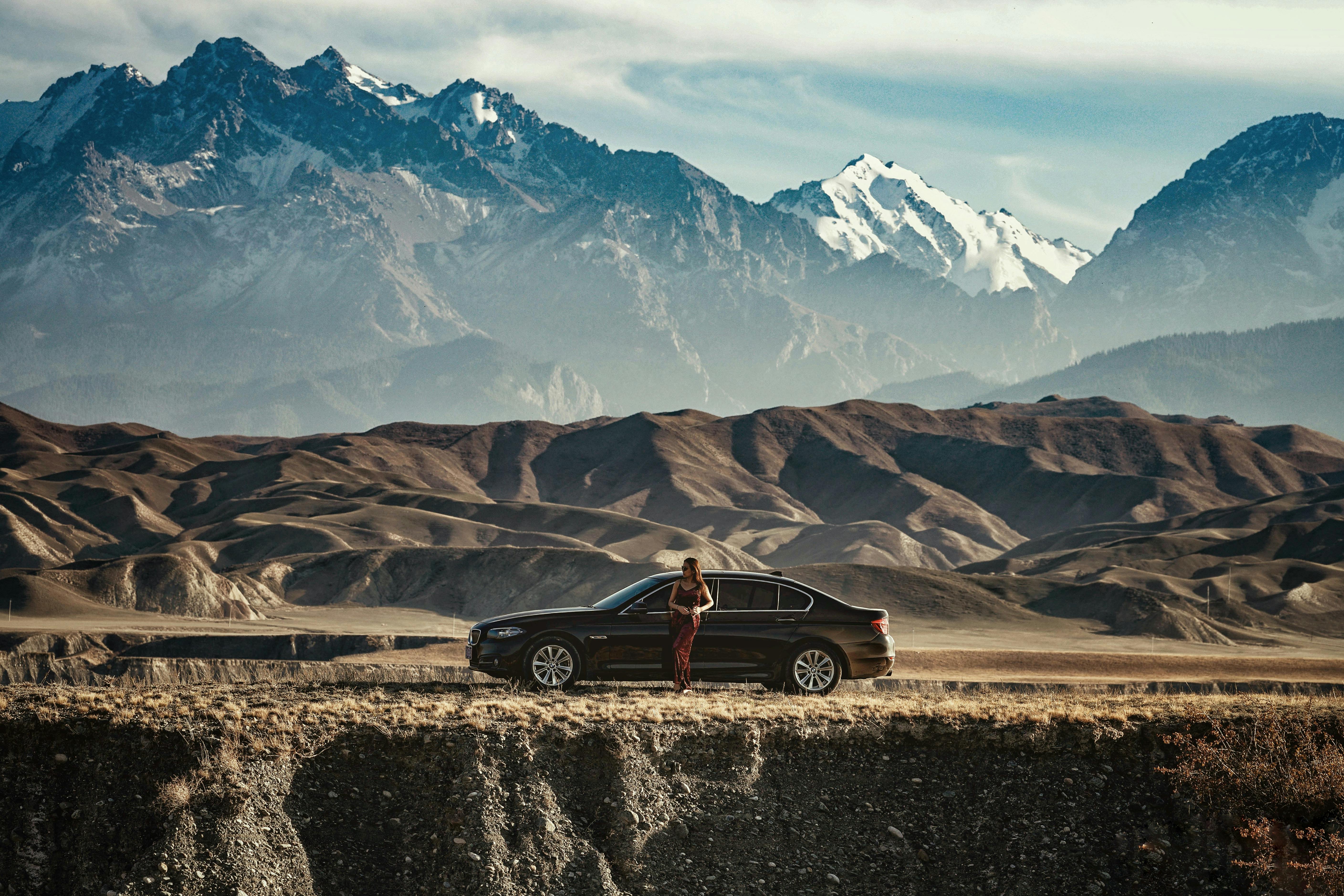 一名女子站在汽车旁，背景是令人惊叹的山脉，体现了探索和旅行精神