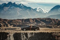 一名女子站在汽车旁，背景是令人惊叹的山脉，体现了探索和旅行精神