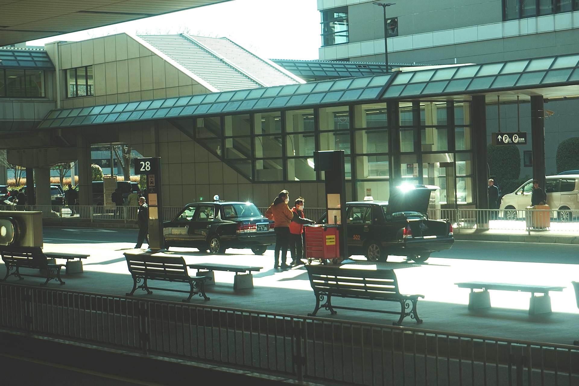 Scene capturing an airport terminal exterior with people interacting and taxis parked at Tokyo airport.