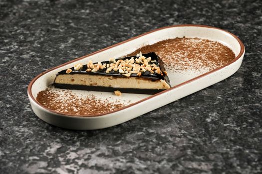A slice of chocolate cake with peanuts on an elegant ceramic dish, perfect for gourmet presentations.