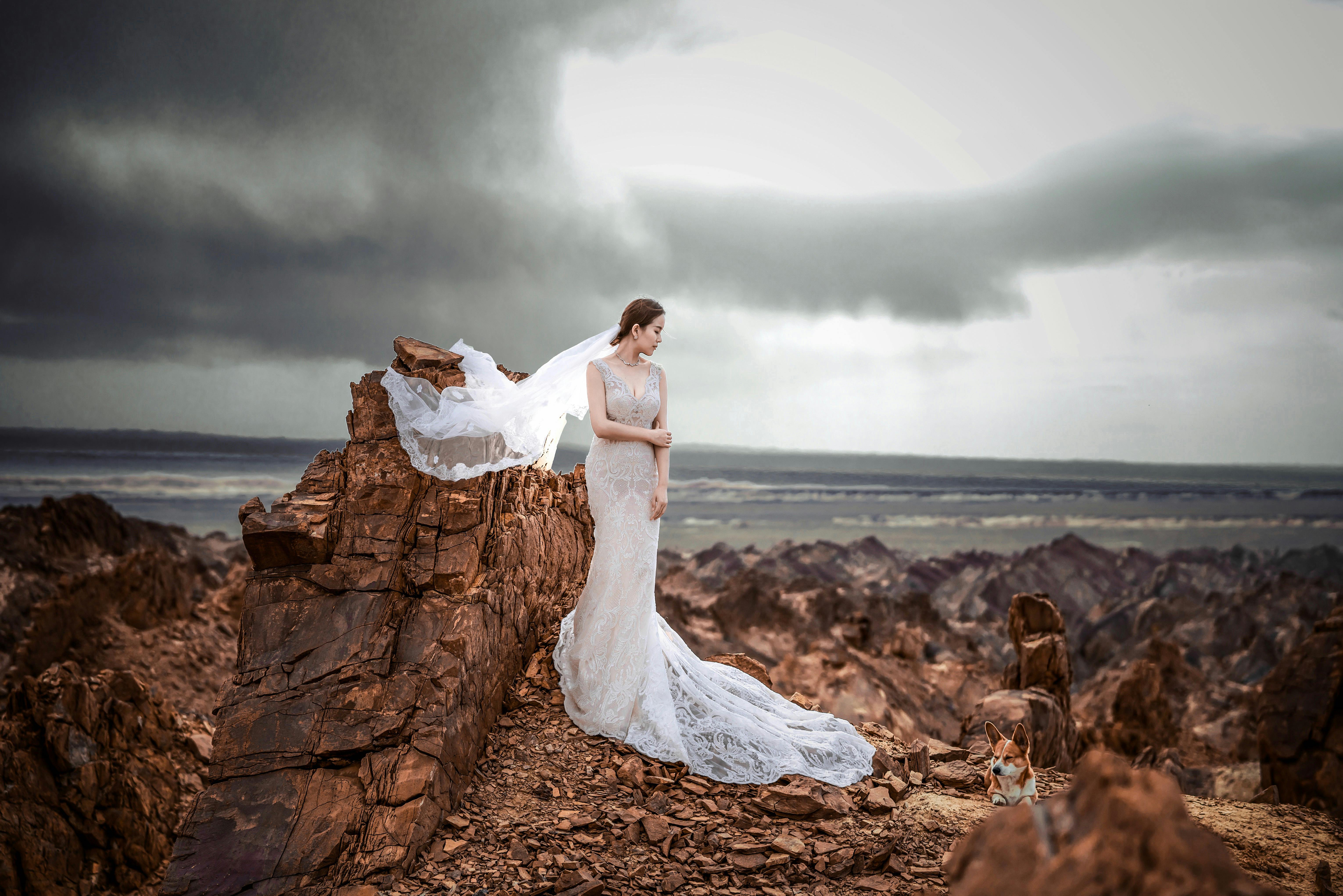 新娘身着飘逸的白色礼服，在变幻的天空下，于嶙峋的岩石景观前摆出姿势