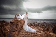 新娘身着飘逸的白色礼服，在变幻的天空下，于嶙峋的岩石景观前摆出姿势