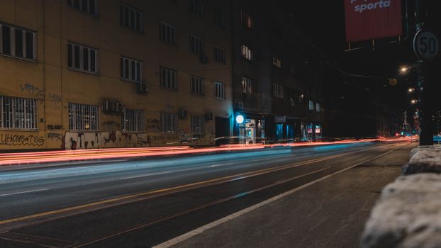 Long exposure of city street at night with vibrant light trails from passing cars.