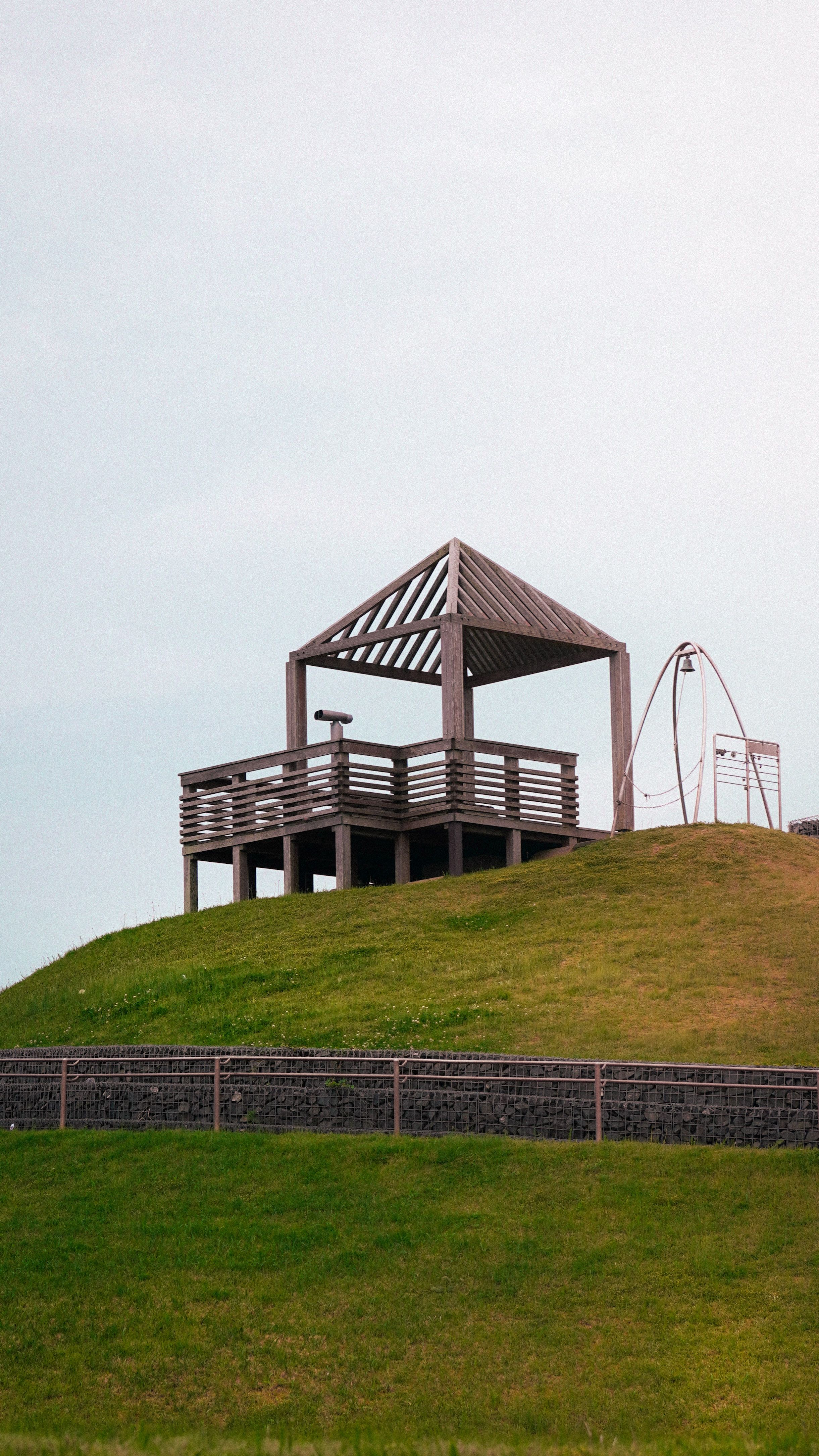 A wooden gazebo on a grassy hilltop with a clear sky background, ideal for outdoor relaxation.