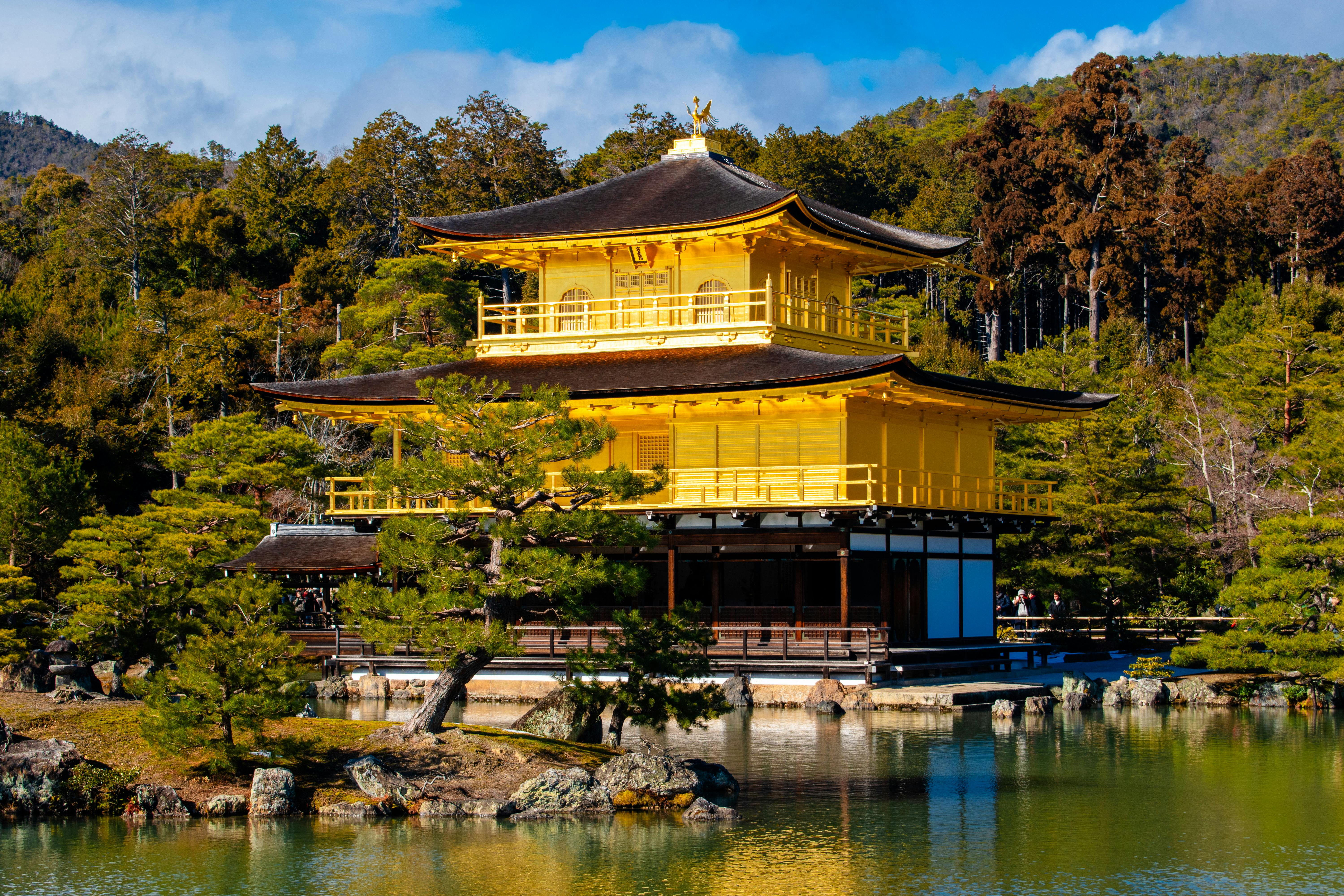 Kinkaku-ji Golden Pavilion reflecting in the serene pond surrounded by lush greenery and traditional Japanese gardens at sunrise