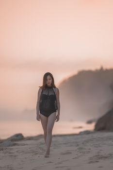 A woman in swimwear walks on a serene beach at sunset, creating a tranquil and picturesque scene.