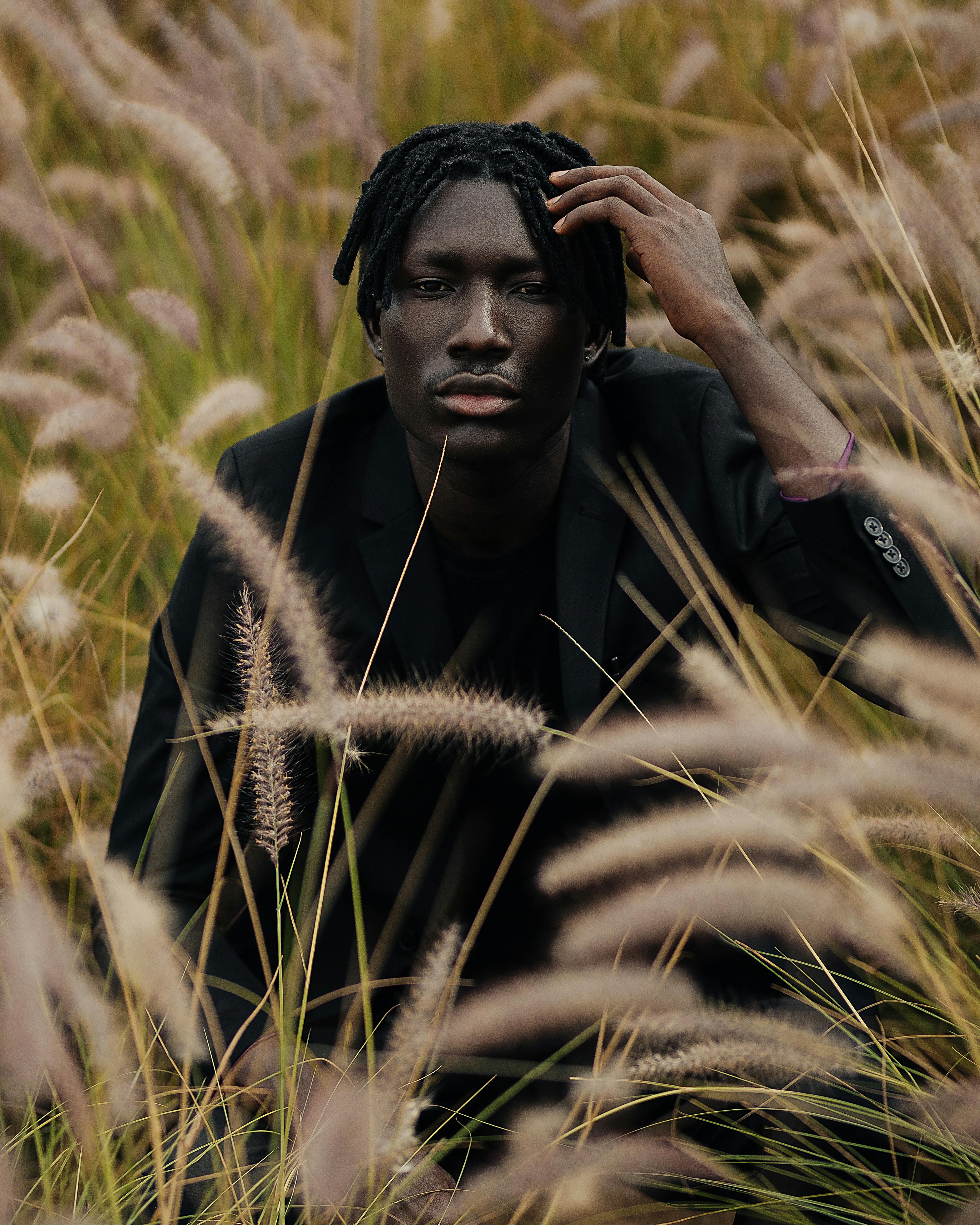 A contemplative man in a black suit surrounded by tall golden grass in Qatar, evoking a serene mood.