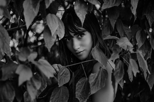 Black and white portrait of a woman surrounded by leaves, creating a mysterious mood.